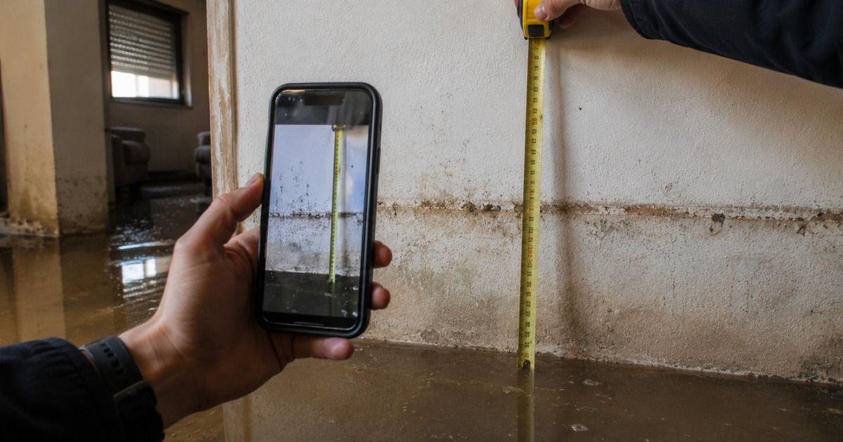 Persona fotografiando con el móvil la altura del agua en la pared de una vivienda inundada